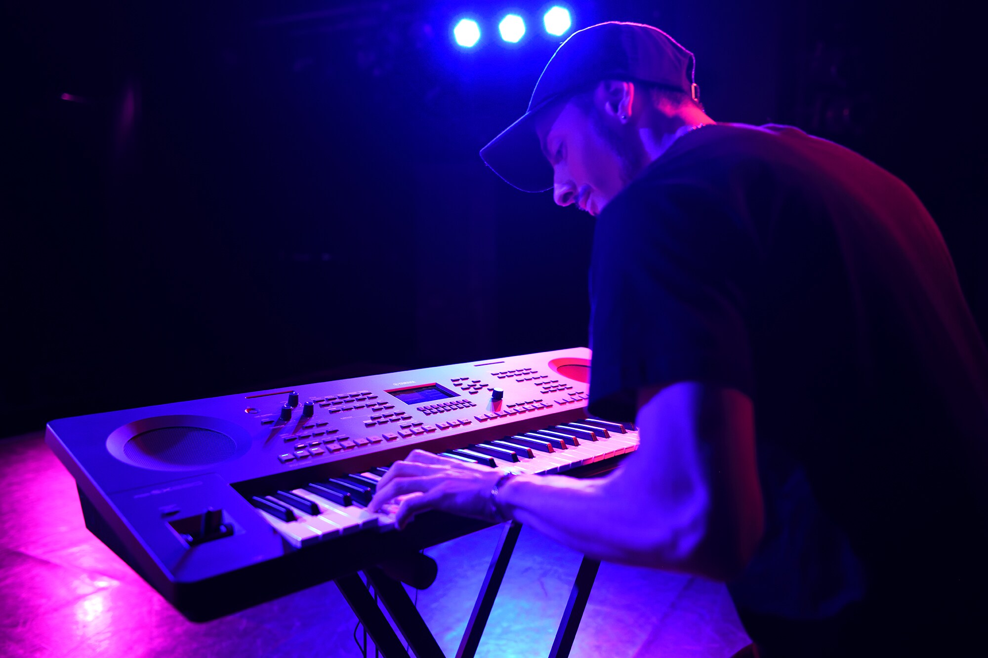 Člověk hrající na aranžovací pracovní stanici Yamaha na stojanu v záři pódiových reflektorů