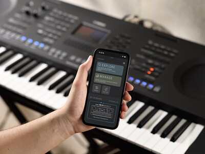 Model PSR-SX620 a ruka držící smartphone s obrazovkou oficiální aplikace Yamaha "Expansion Explorer".