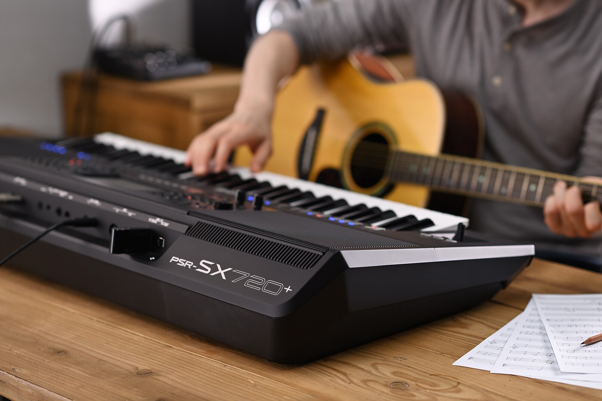 Fotografie člověka, který hraje na aranžovací pracovní stanici Yamaha PSR-SX720+ a drží přitom kytaru