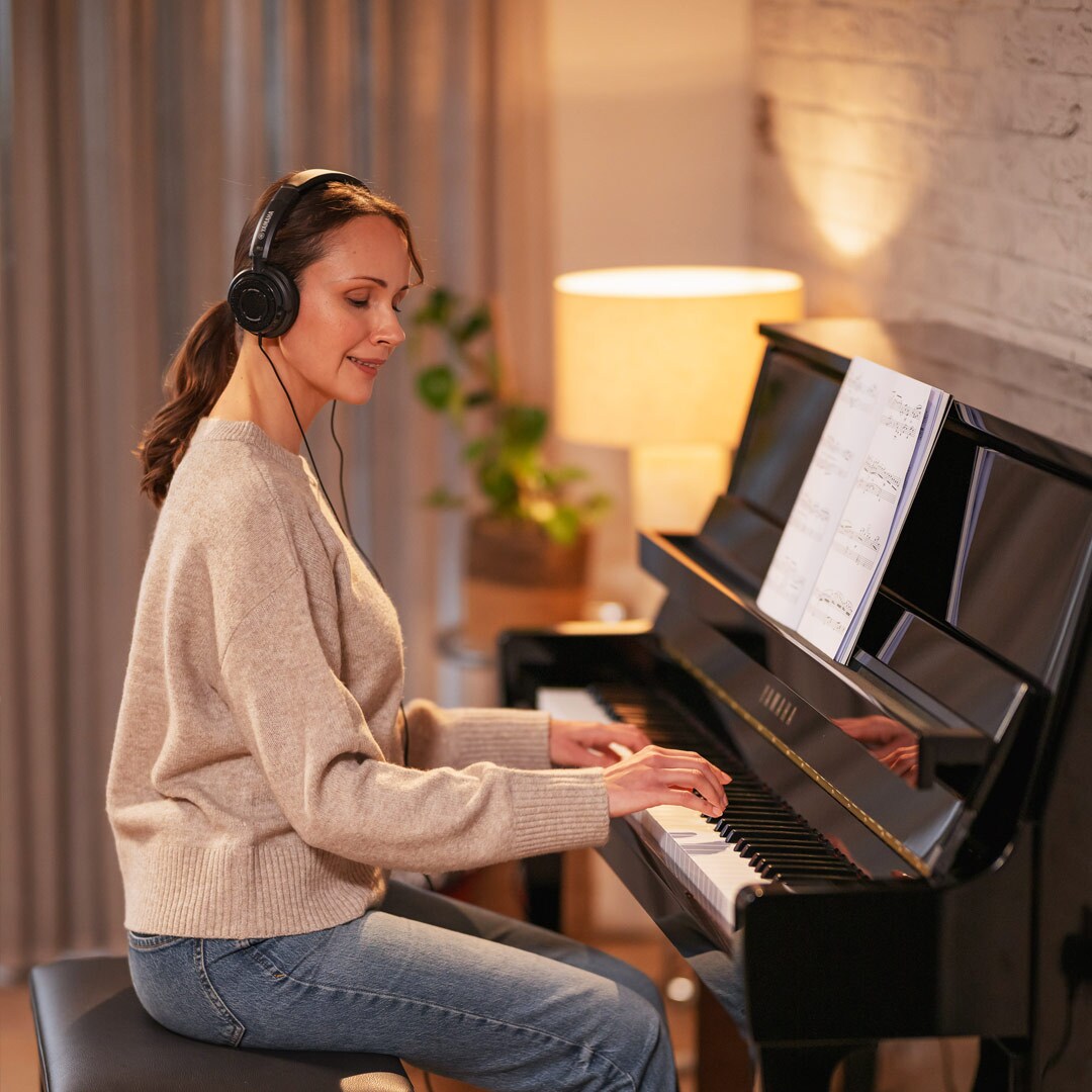 Žena si s potěšením hraje na piano se sluchátky na uších